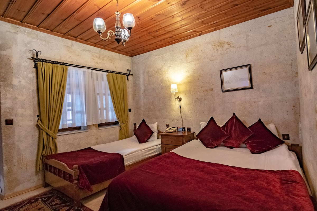 Quarto com duas camas, teto de madeira, um candelabro, mesa de cabeceira com abajur e um quadro emoldurado na parede.