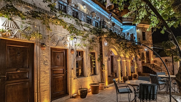 A courtyard with stone walls, wooden doors, and potted plants. There are outdoor tables and chairs. - Goreme House Hotel (Nevsehir)
