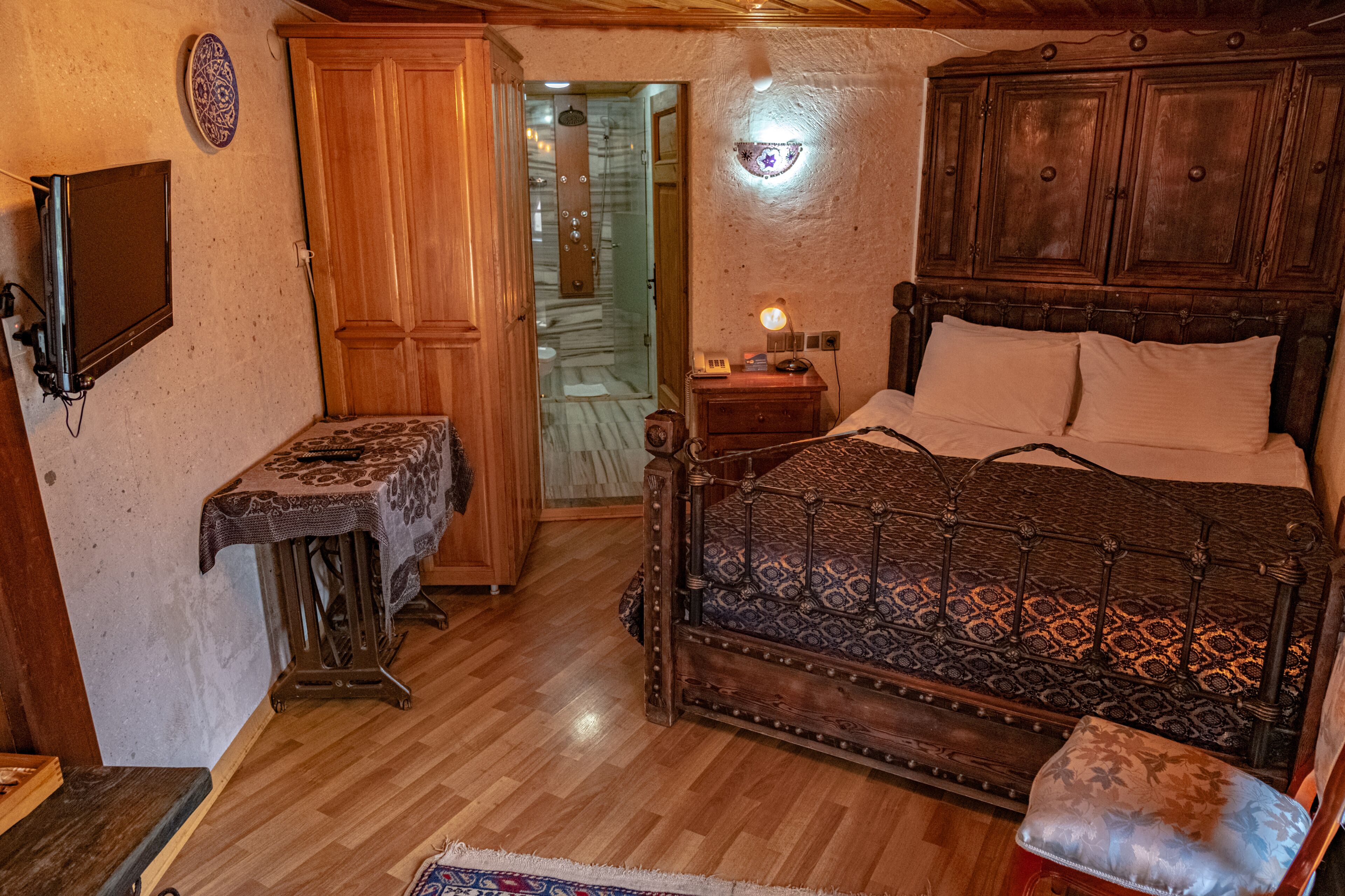 Een slaapkamer met een houten bed, een nachtkastje, een wandtelevisie en een deur naar een badkamer.