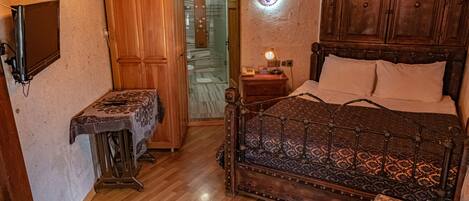 A bedroom with a wooden bed, a bedside table, a nightstand, a wall-mounted TV, and a door leading to a bathroom.