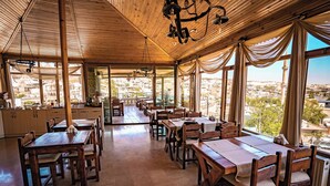 A restaurant with wooden furniture and large windows offering a city view. - Goreme House Hotel (Nevsehir)