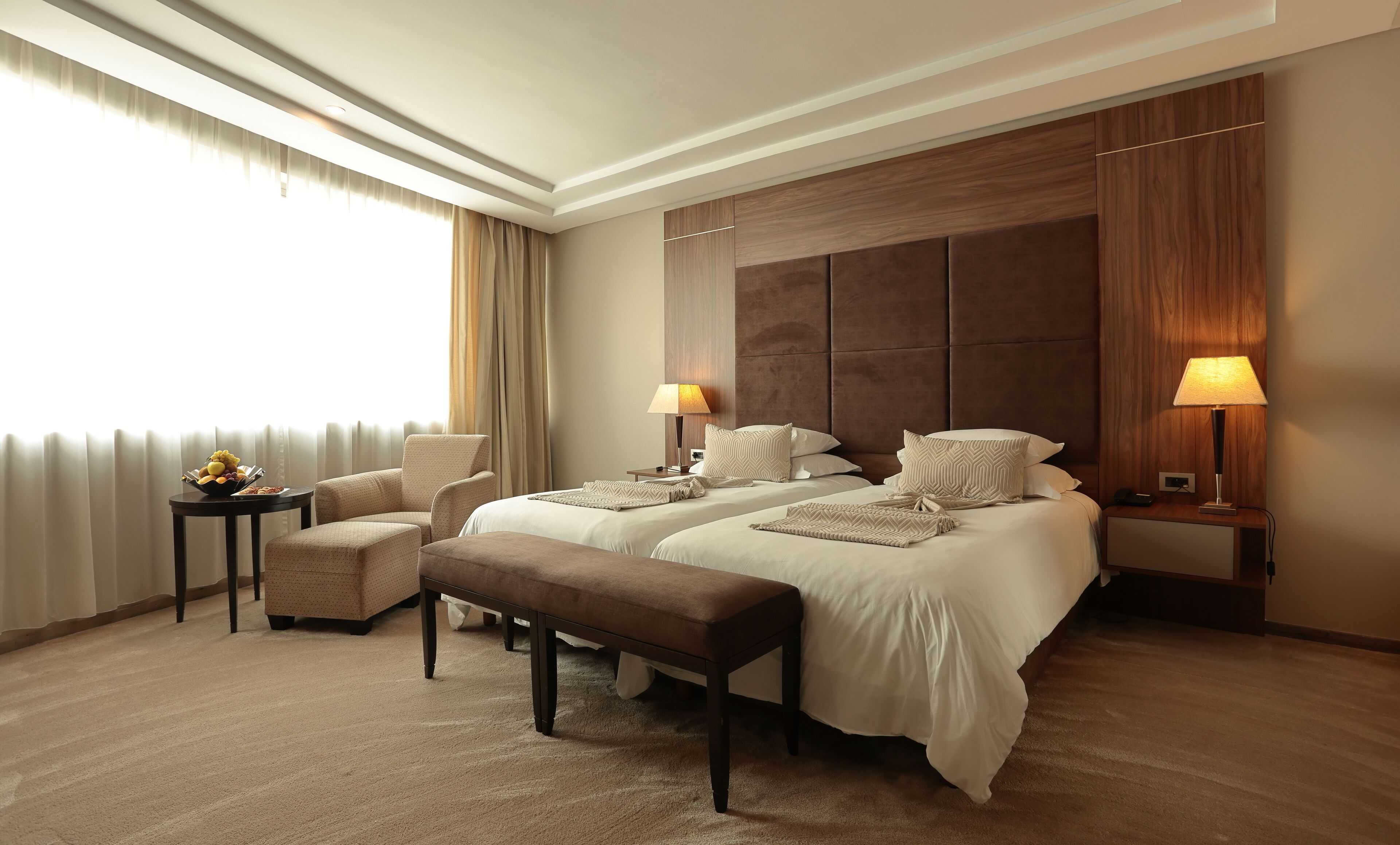 Habitación de hotel con dos camas, una zona de estar con una silla, una mesita y una lámpara.