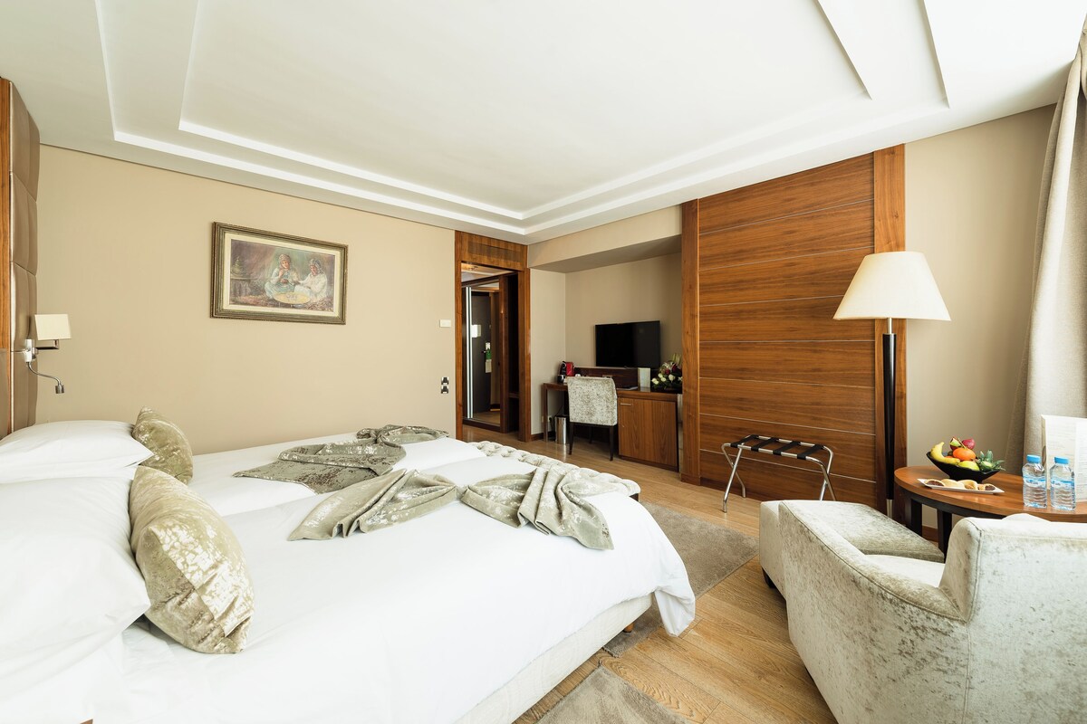 A hotel room with a bed, a desk, a chair, a TV, and a painting on the wall.