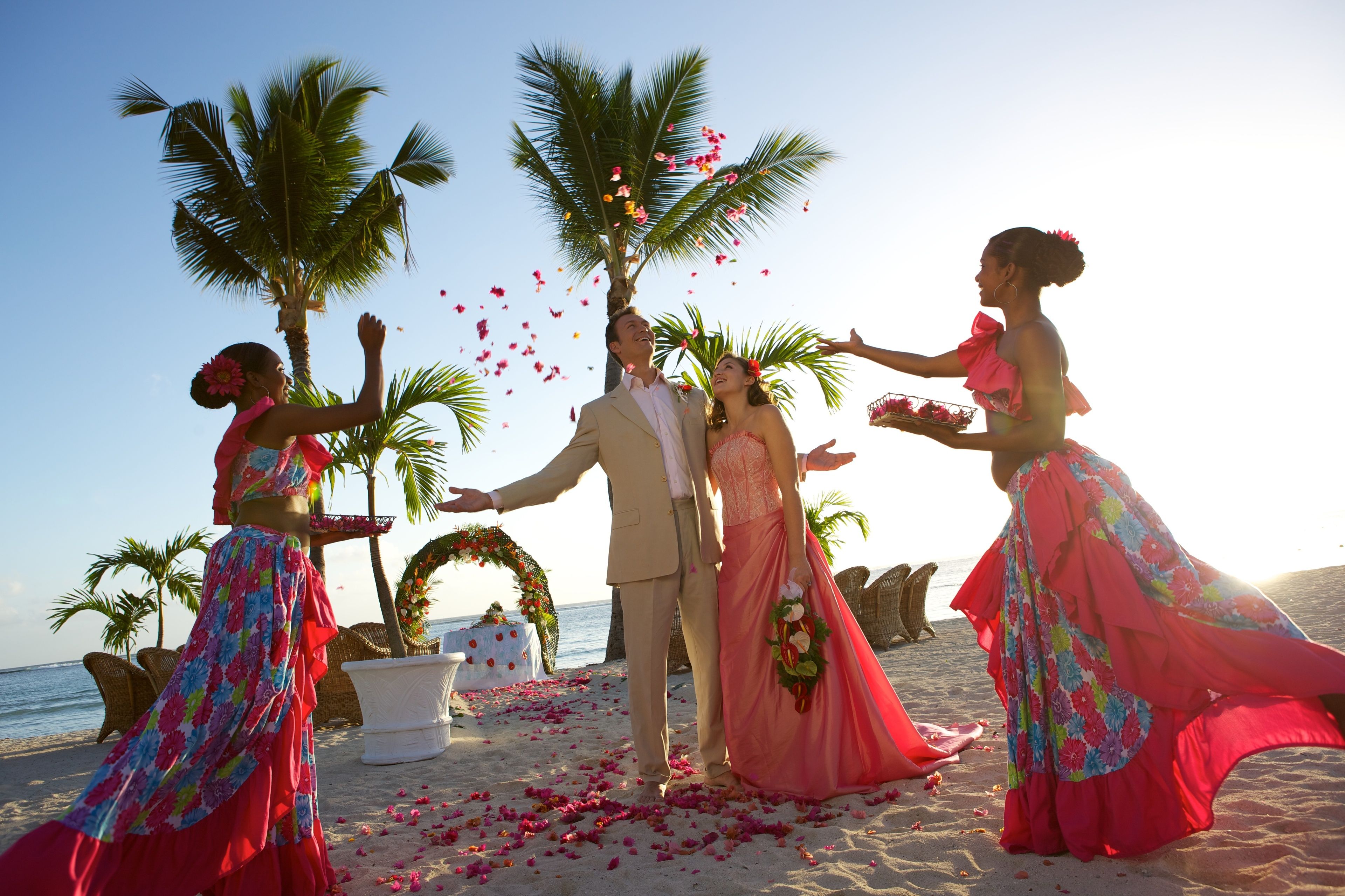 A wedding ceremony on a beach with palm trees and a decorated arch.