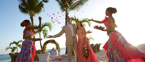 A wedding ceremony on a beach with palm trees and a decorated arch.