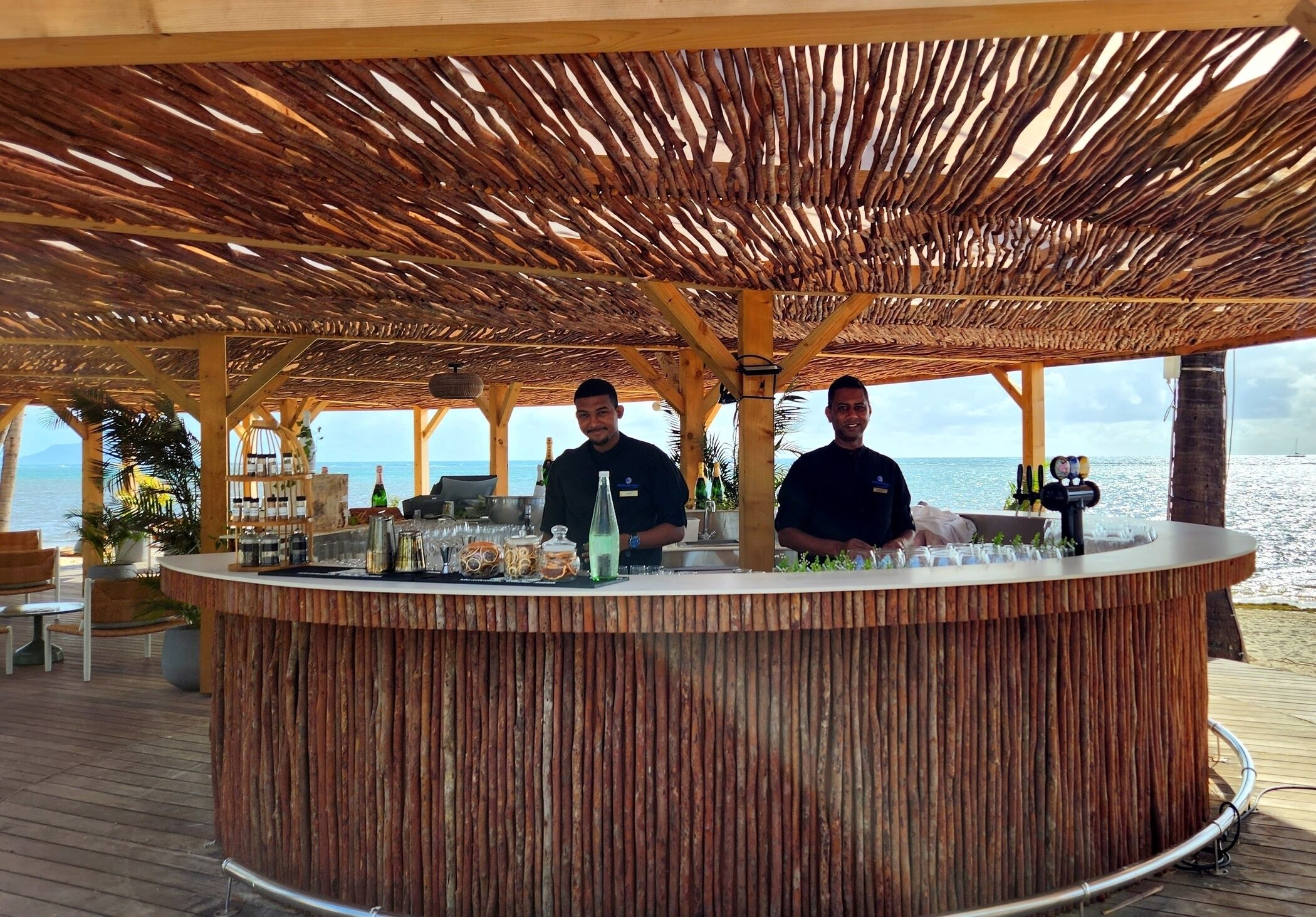 A wooden bar area with two staff members, overlooking a body of water.
