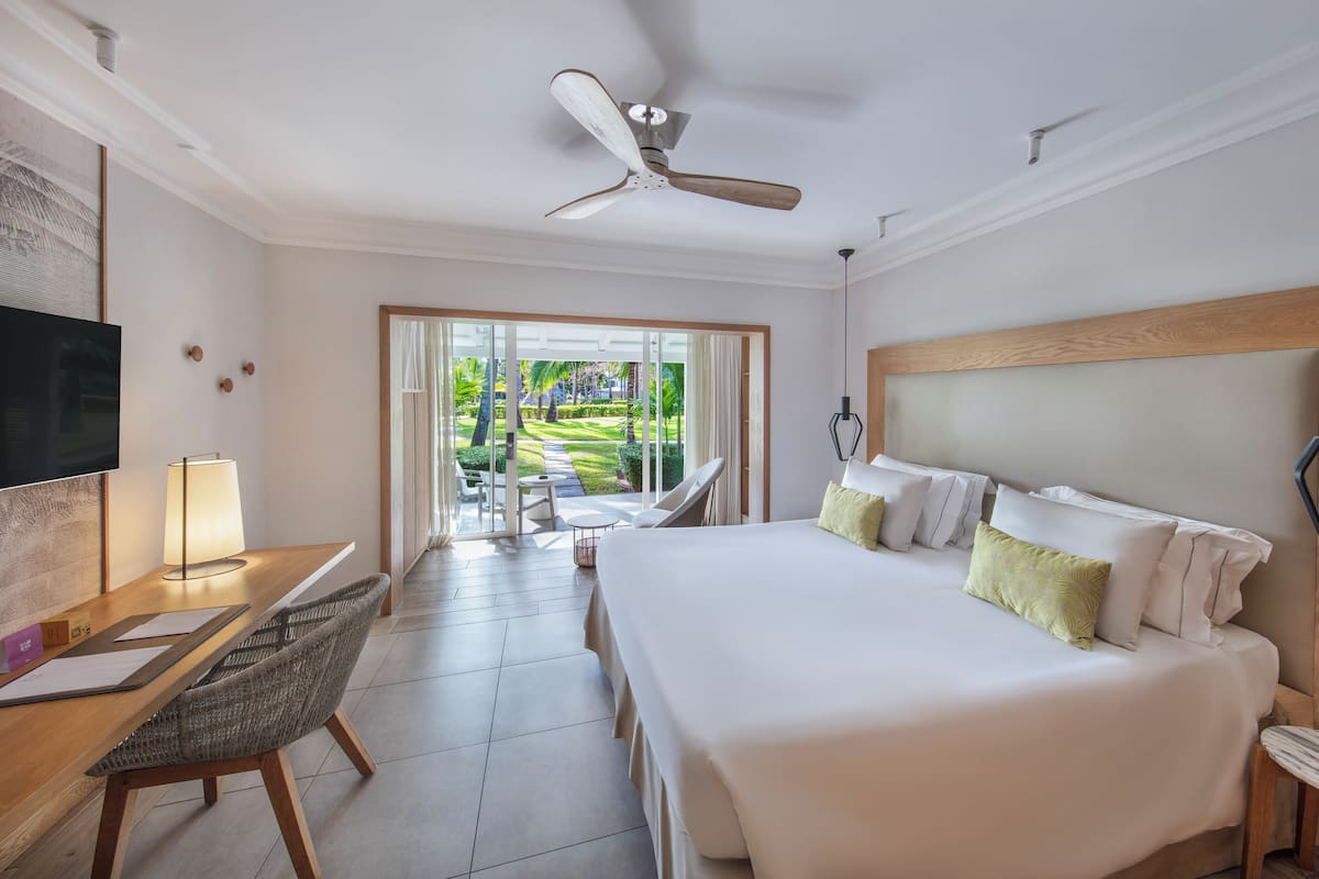 Habitación de hotel con una cama grande, un escritorio con una silla, televisión y vistas a un jardín desde la ventana.