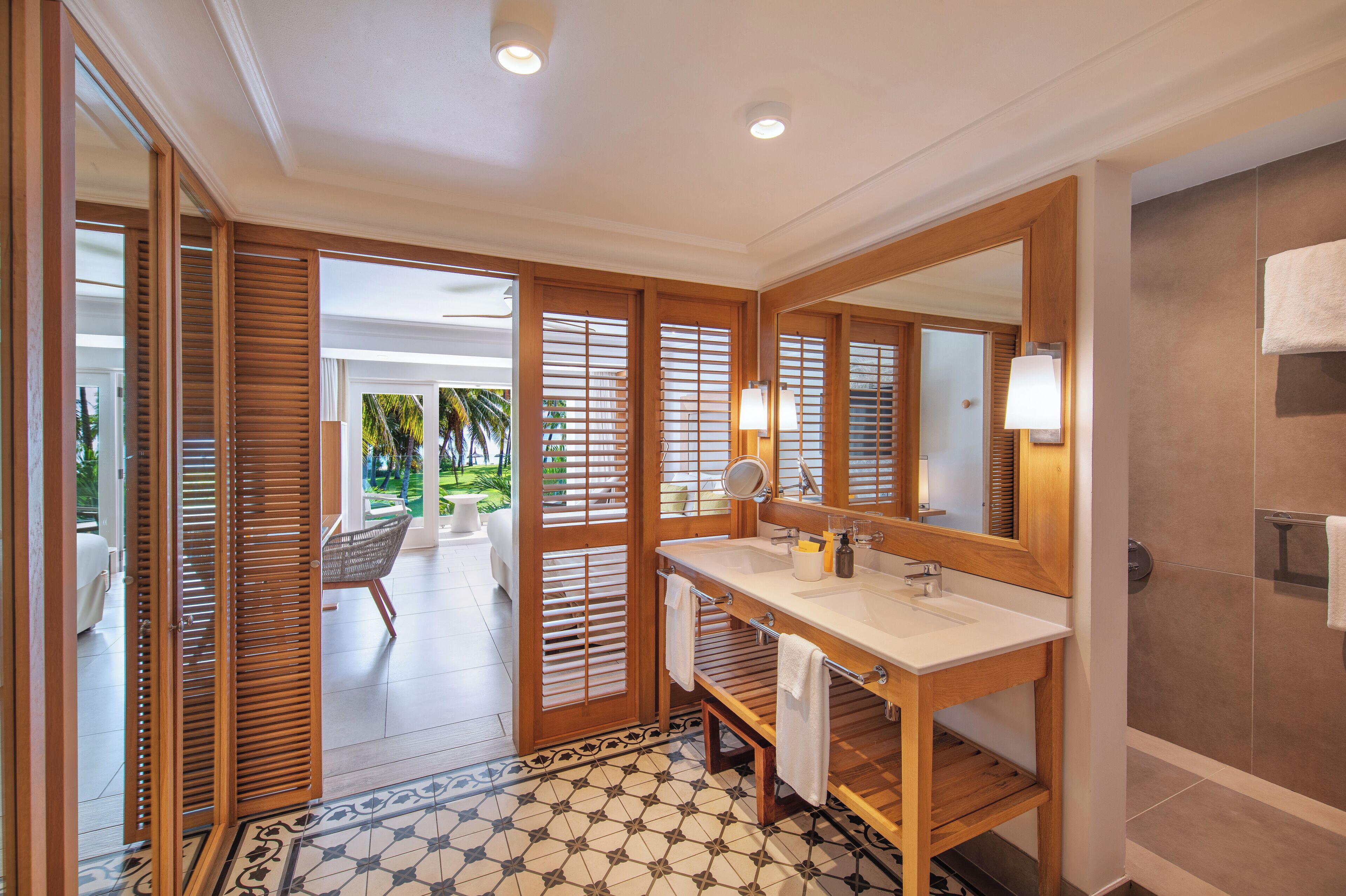 A bathroom with a large mirror, wooden door, and a view of a balcony.