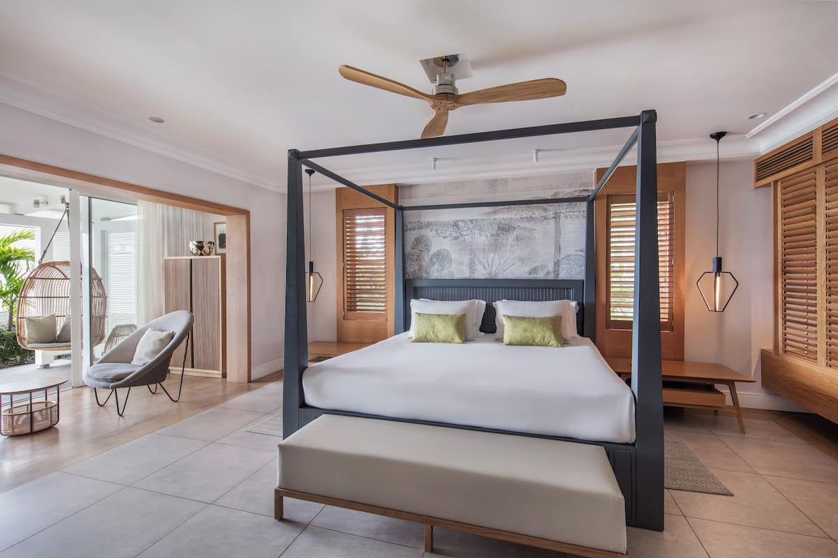 Un dormitorio amplio con cama con dosel, ventilador de techo y un ventanal con persianas.