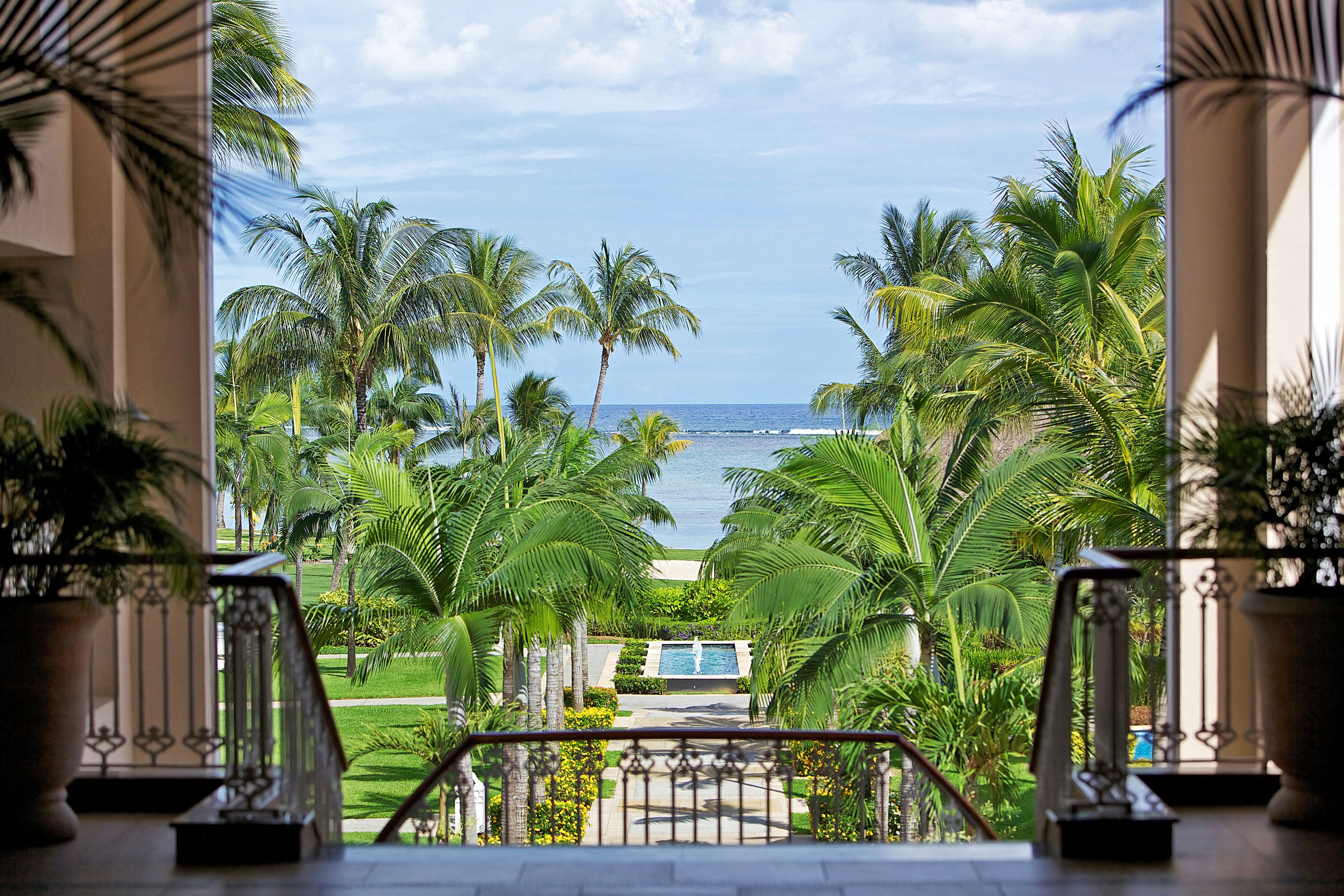 A view from a balcony overlooking a pool, palm trees, and the ocean.