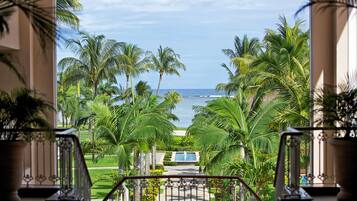 A view from a balcony overlooking a pool, palm trees, and the ocean.