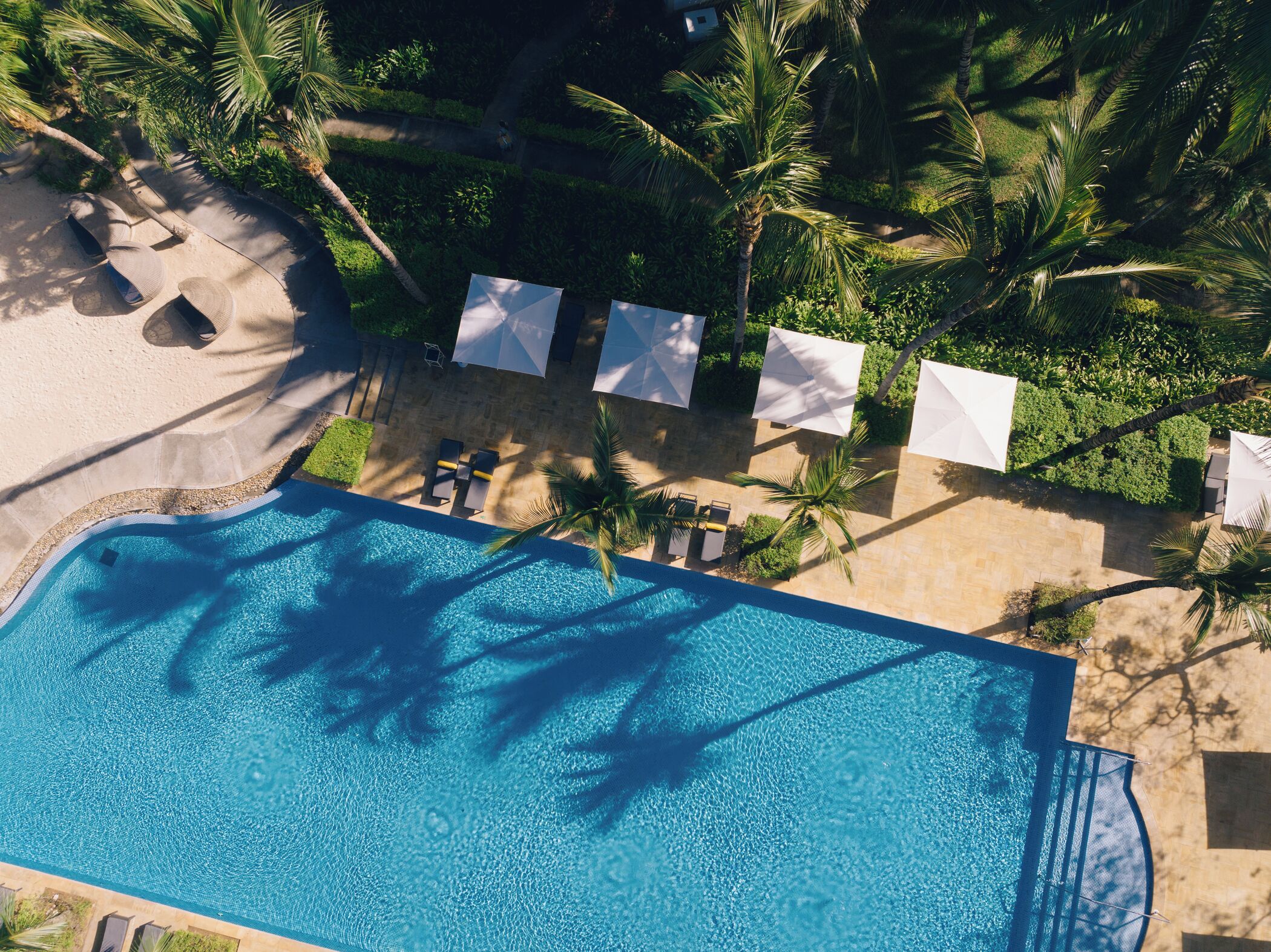 Vista aérea de um resort com piscina, espreguiçadeiras e guarda-sóis.