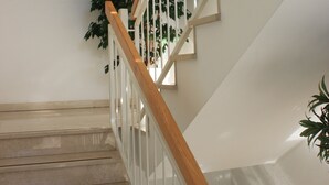 Una escalera con barandillas de madera y pasamanos blancos, que conduce a un rellano con una lámpara en el techo.