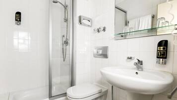 Un baño moderno con cabina de ducha de vidrio, inodoro, lavabo y espejo con repisa de vidrio arriba.