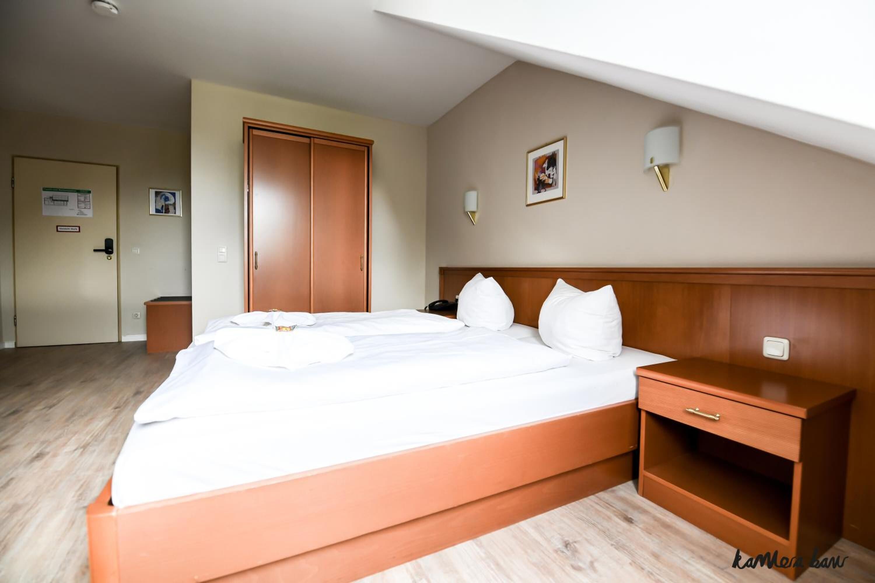 A hotel room with a large bed, wooden headboard, bedside tables, and a wardrobe.