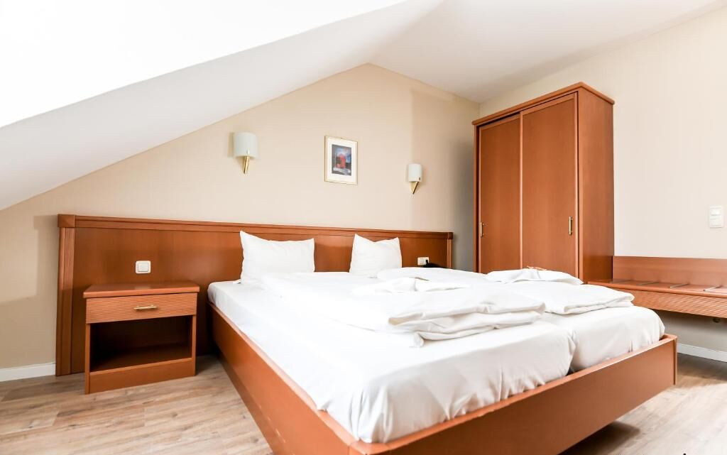 A bedroom with a wooden bed, nightstands, a wardrobe, and a sloped ceiling.