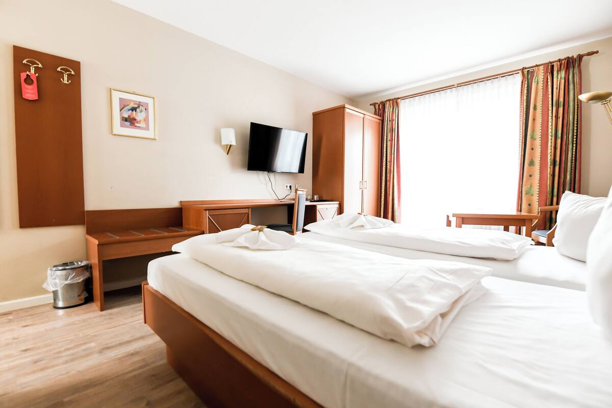Habitación de hotel con dos camas, un escritorio, un televisor y una ventana con cortinas.