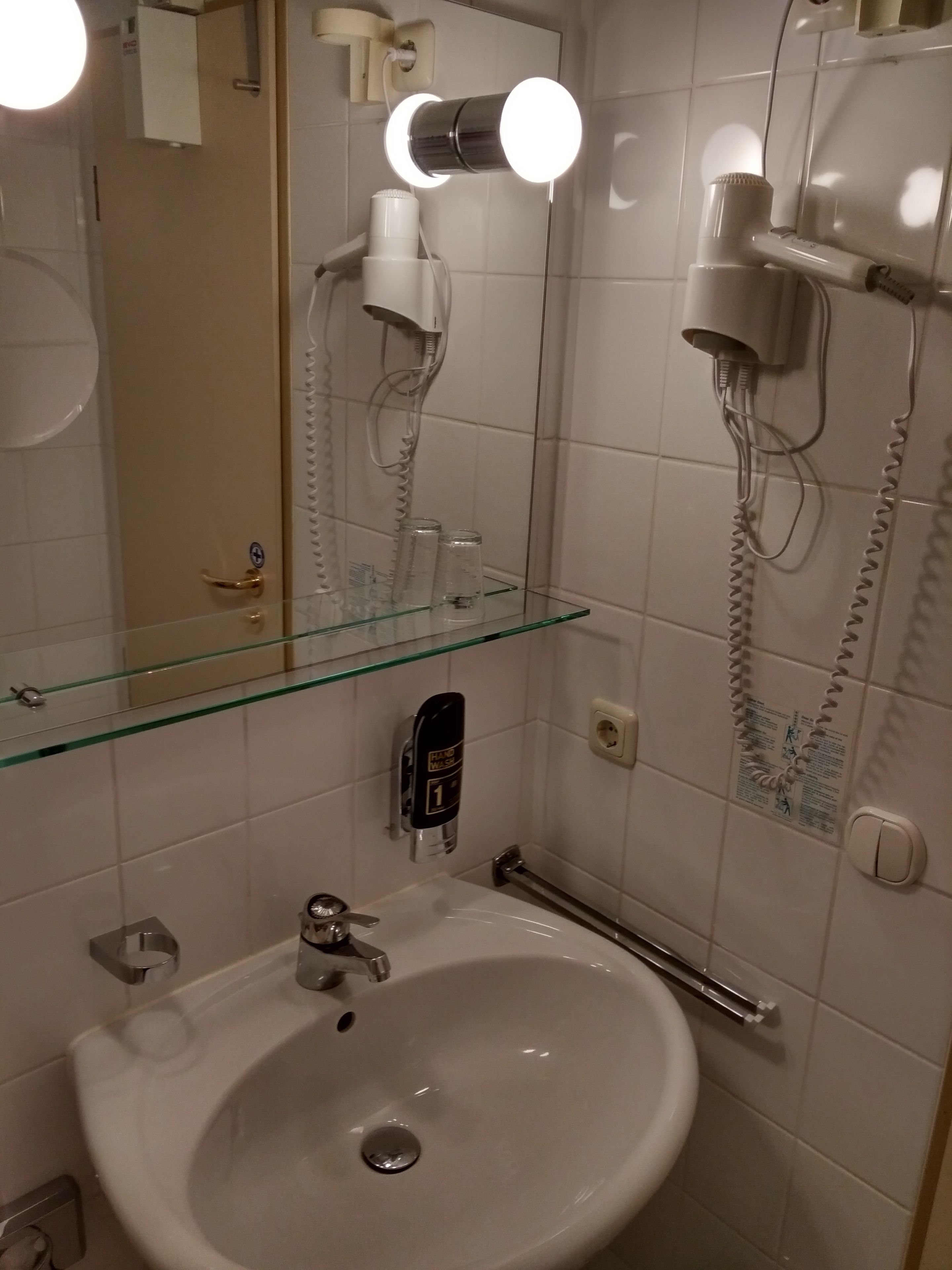 A bathroom with a sink, mirror, hairdryer, and a glass shelf.