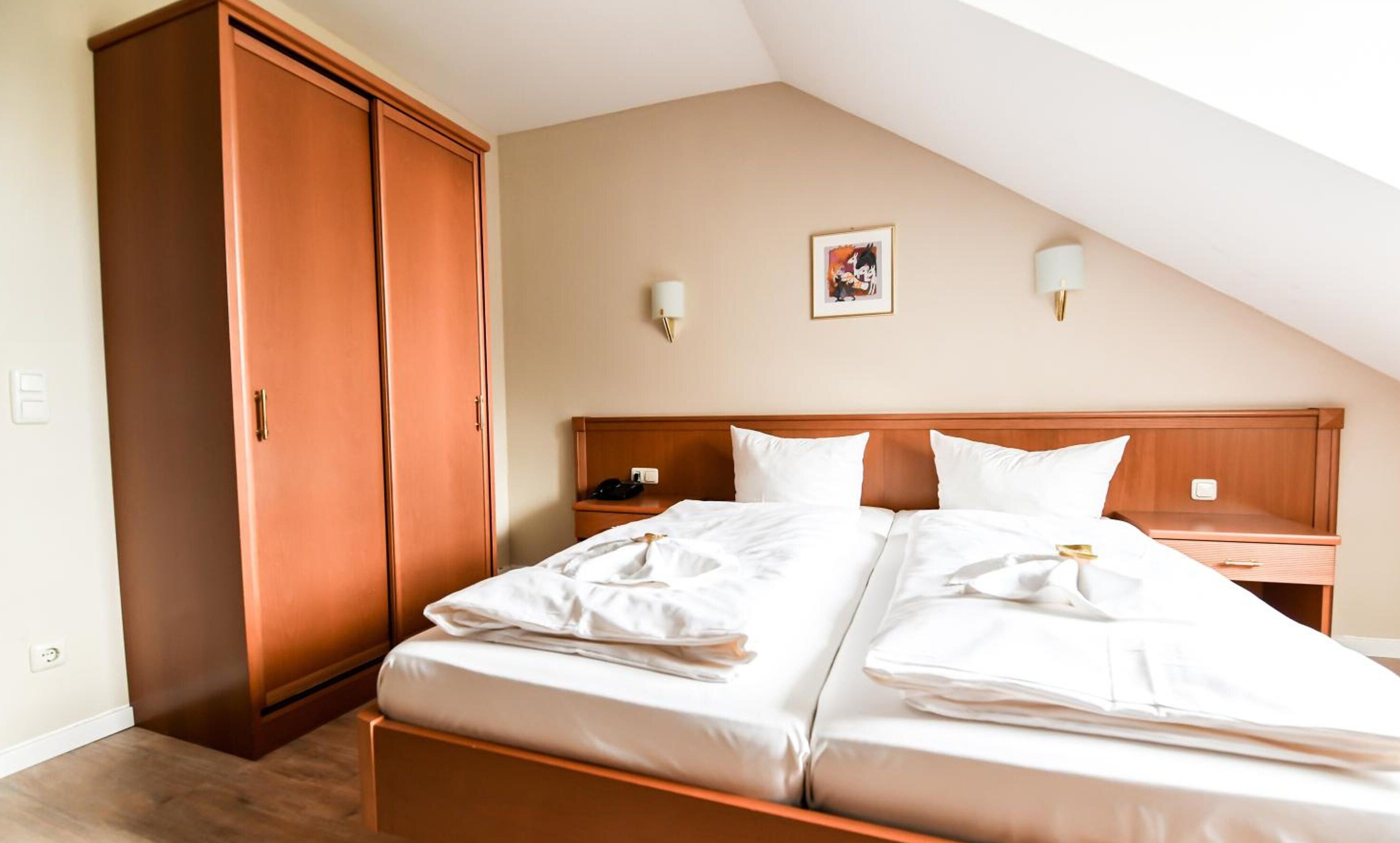 A hotel room with a double bed, a wardrobe, a bedside table, and two wall-mounted lamps.