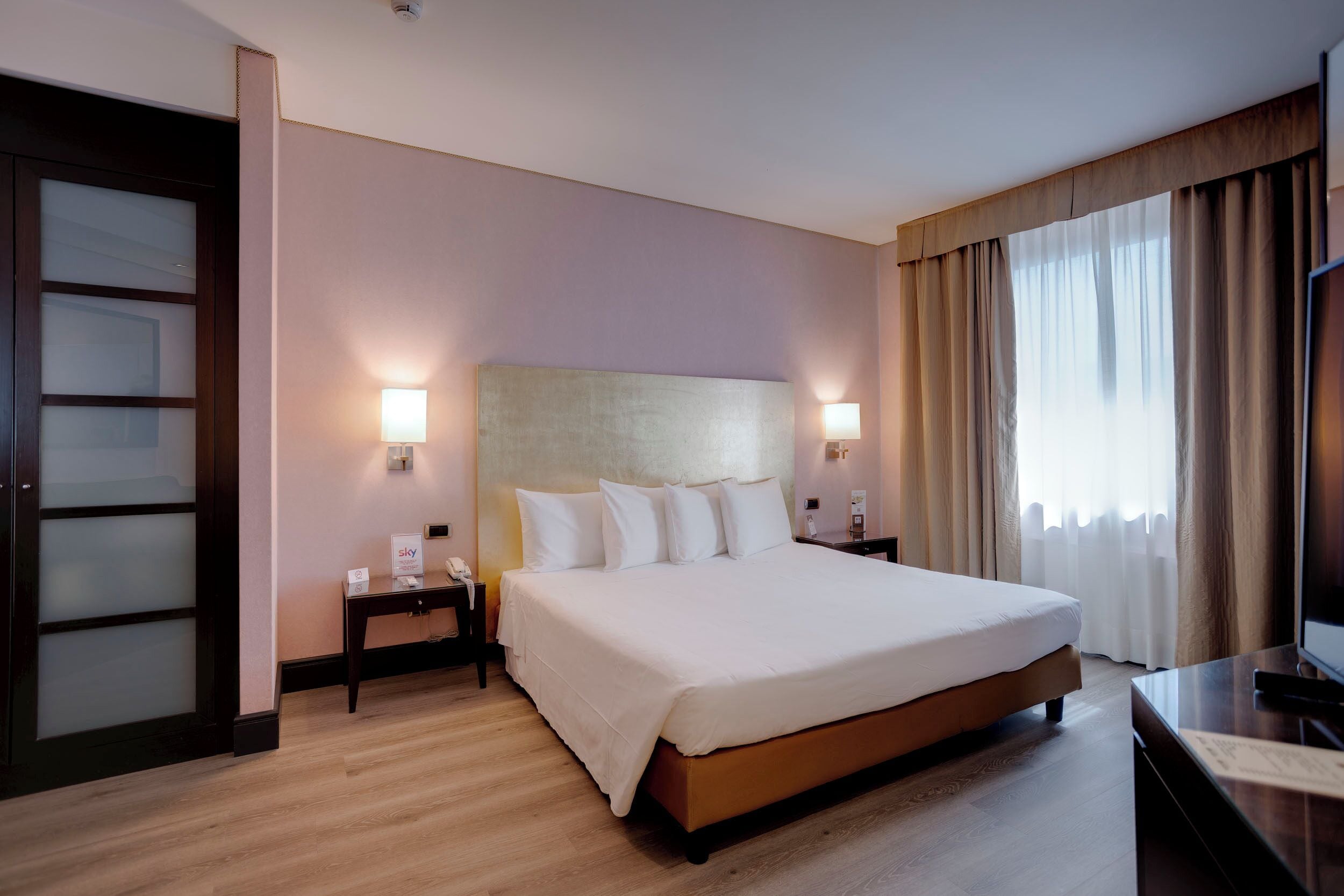 Una habitación de hotel con una cama grande, lámparas de noche, un escritorio y un televisor.