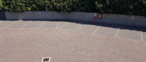 A paved parking area with a brick pattern, a wall with trees, and a red fire hydrant.