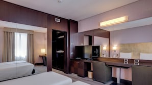 Una habitación de hotel con cama, escritorio con computadora, televisor y espejo.