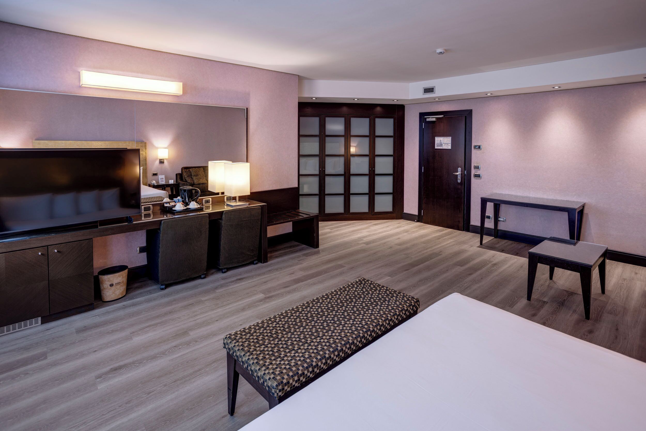 A hotel room with a bed, a desk with a chair, a television, and a small table.