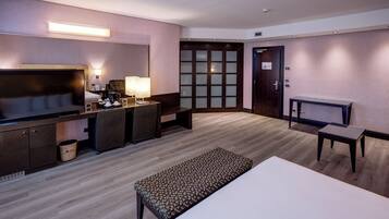 A hotel room with a bed, a desk with a chair, a television, and a small table.