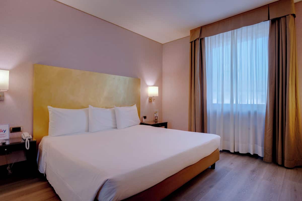 Ein großes Bett mit weißen Leinen, ein Nachttisch mit Lampe und ein Telefon.