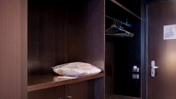 Een moderne hotelkamer met een inbouwkleerkast, een nachtkastje met een kussen, en een houten vloer.