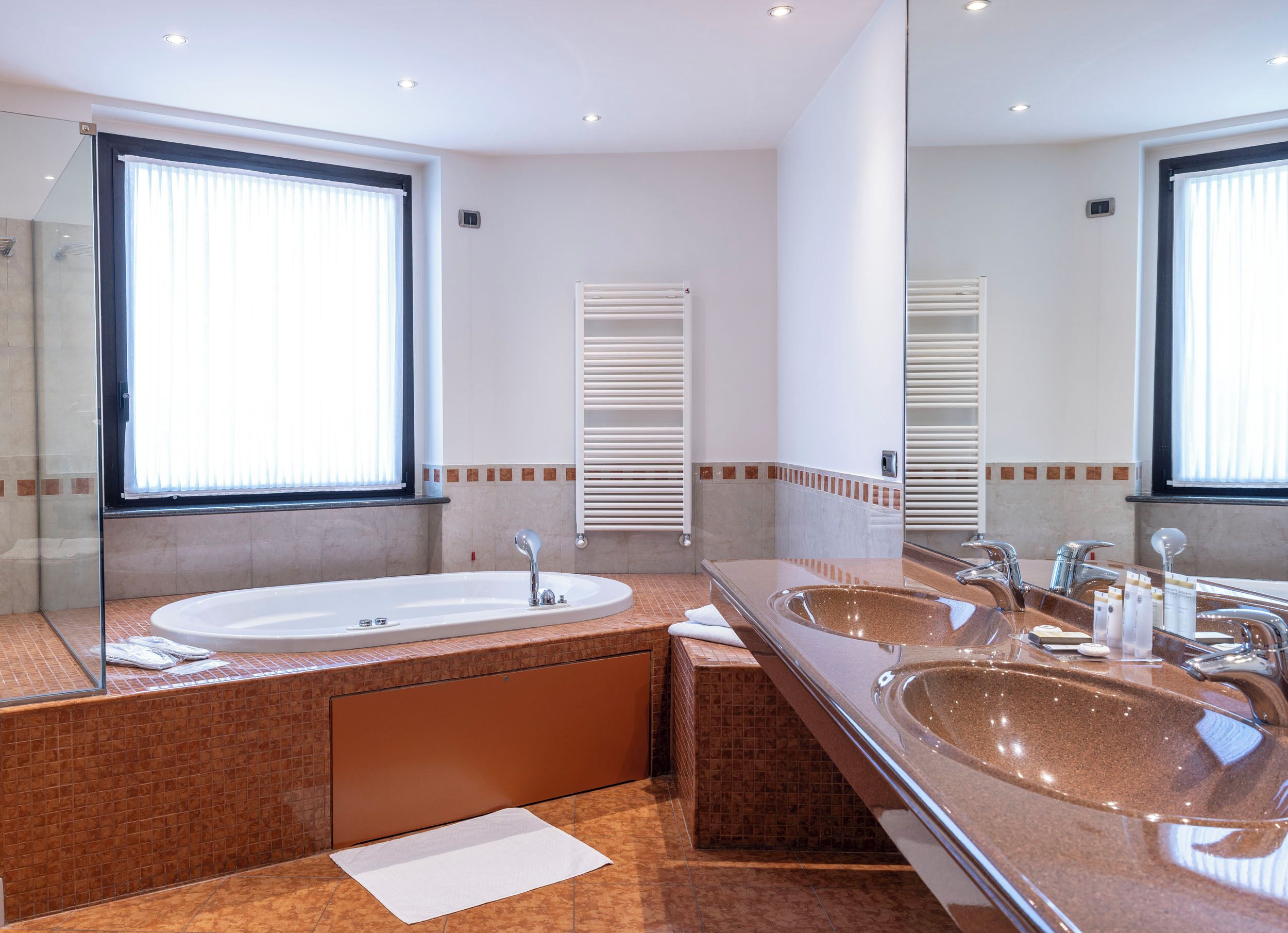 A modern bathroom with two sinks, a large mirror, and a window with blinds.
