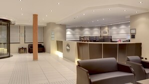 Un moderno vestíbulo de hotel con mostrador de recepción, zona de estar y un pilar grande.