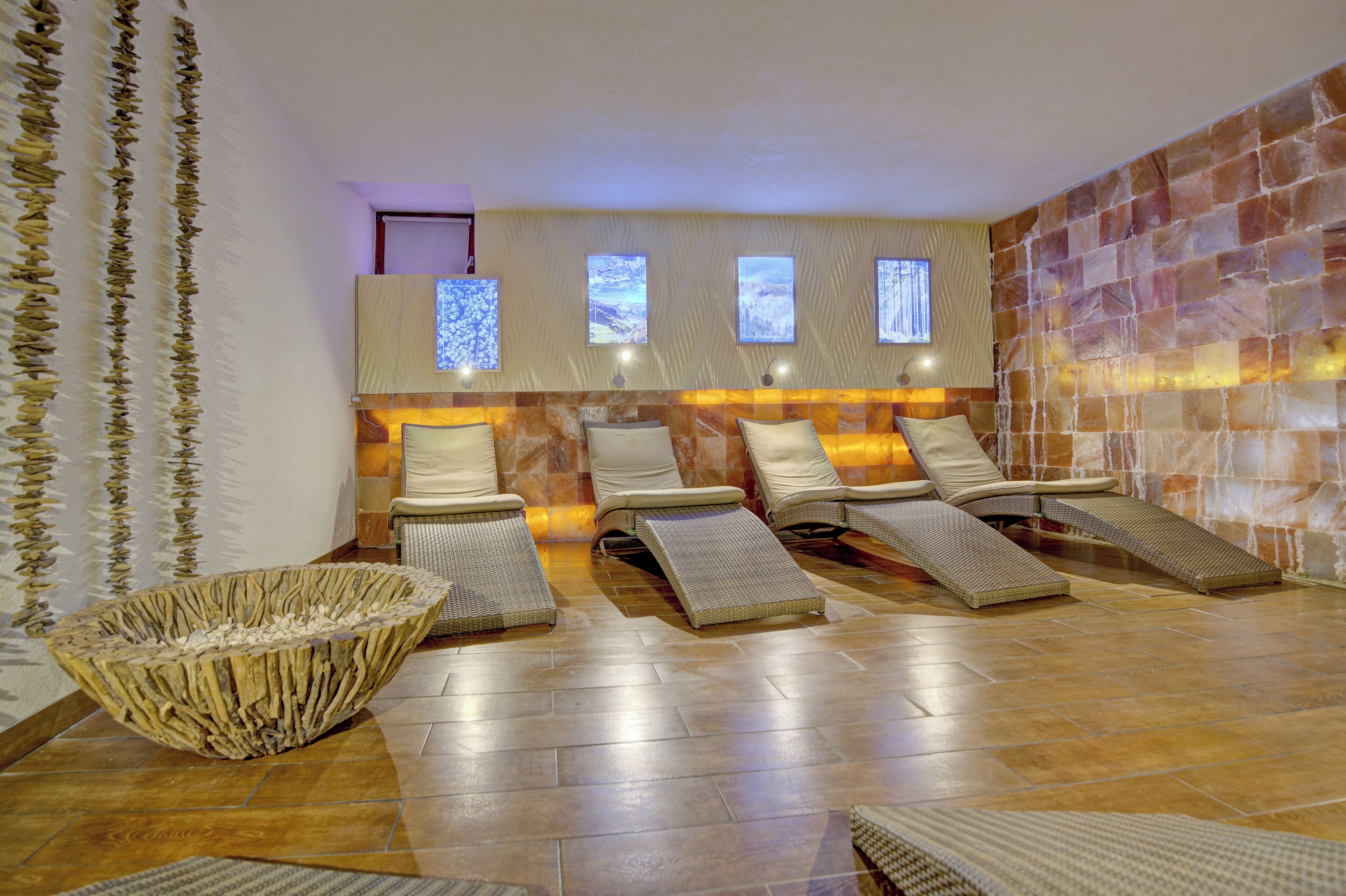 Une salle de spa équipée de trois fauteuils inclinables, d’un grand récipient en fibres tressées et d’un mur en pierre agrémenté de fenêtres.