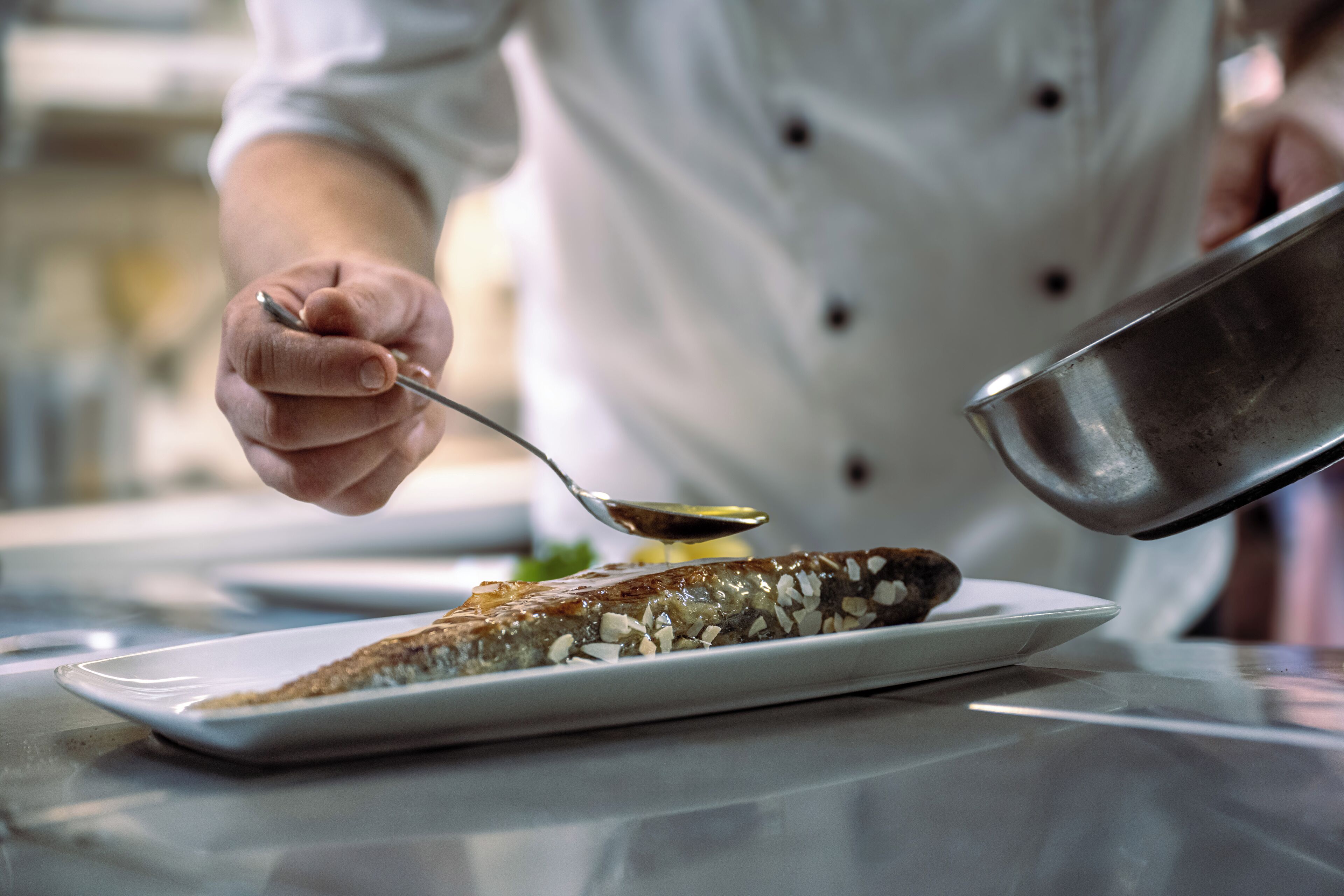 A chef pouring sauce onto a dish.