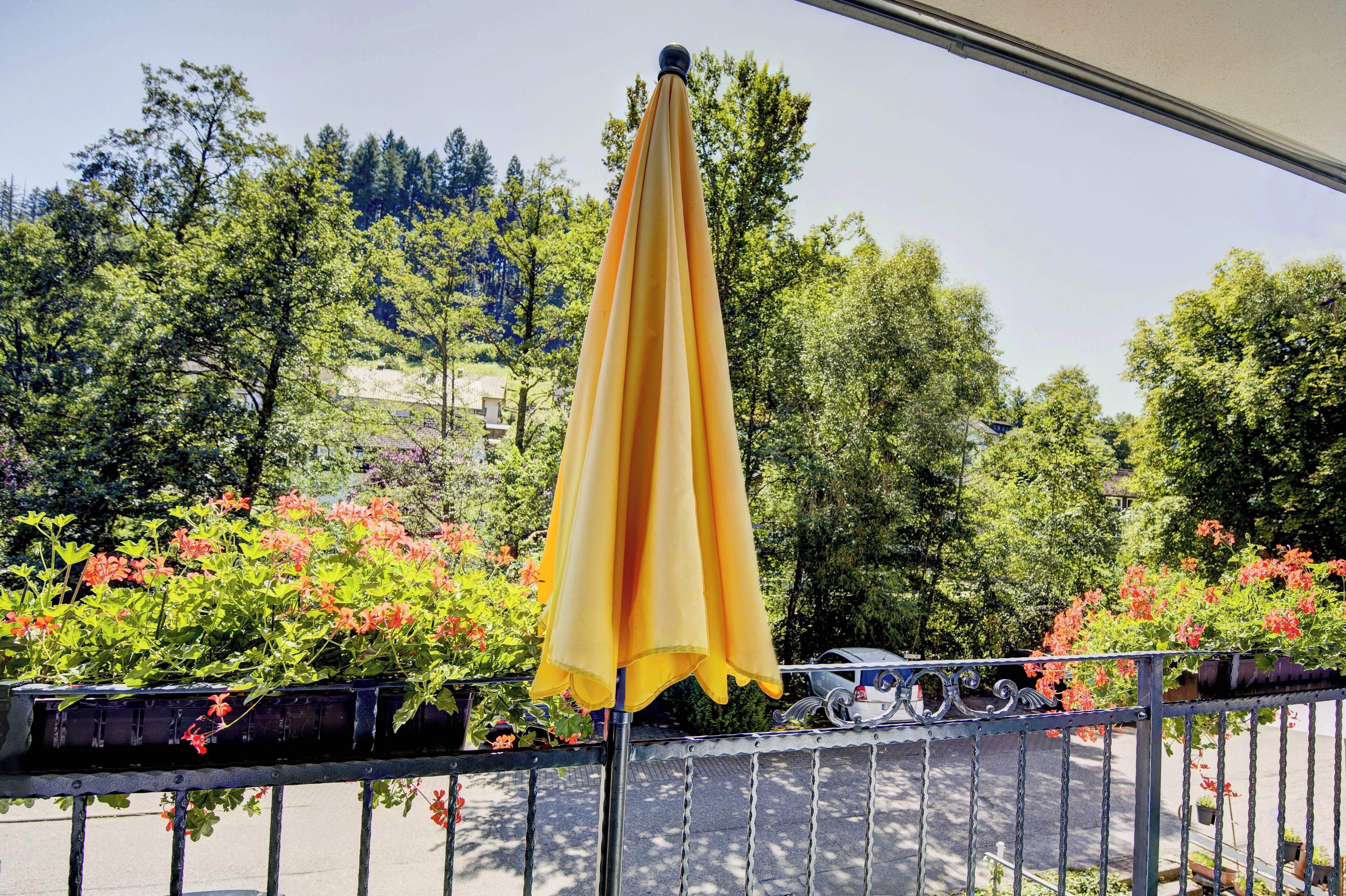 An outdoor area with a yellow umbrella, metal railing, and potted plants with red flowers.