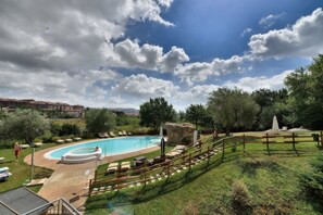 A swimming pool with a waterfall feature, surrounded by a wooden deck and lounge chairs, set against a backdrop of trees and a clear sky. - La Meridiana Bleisure Hotel (Perugia)