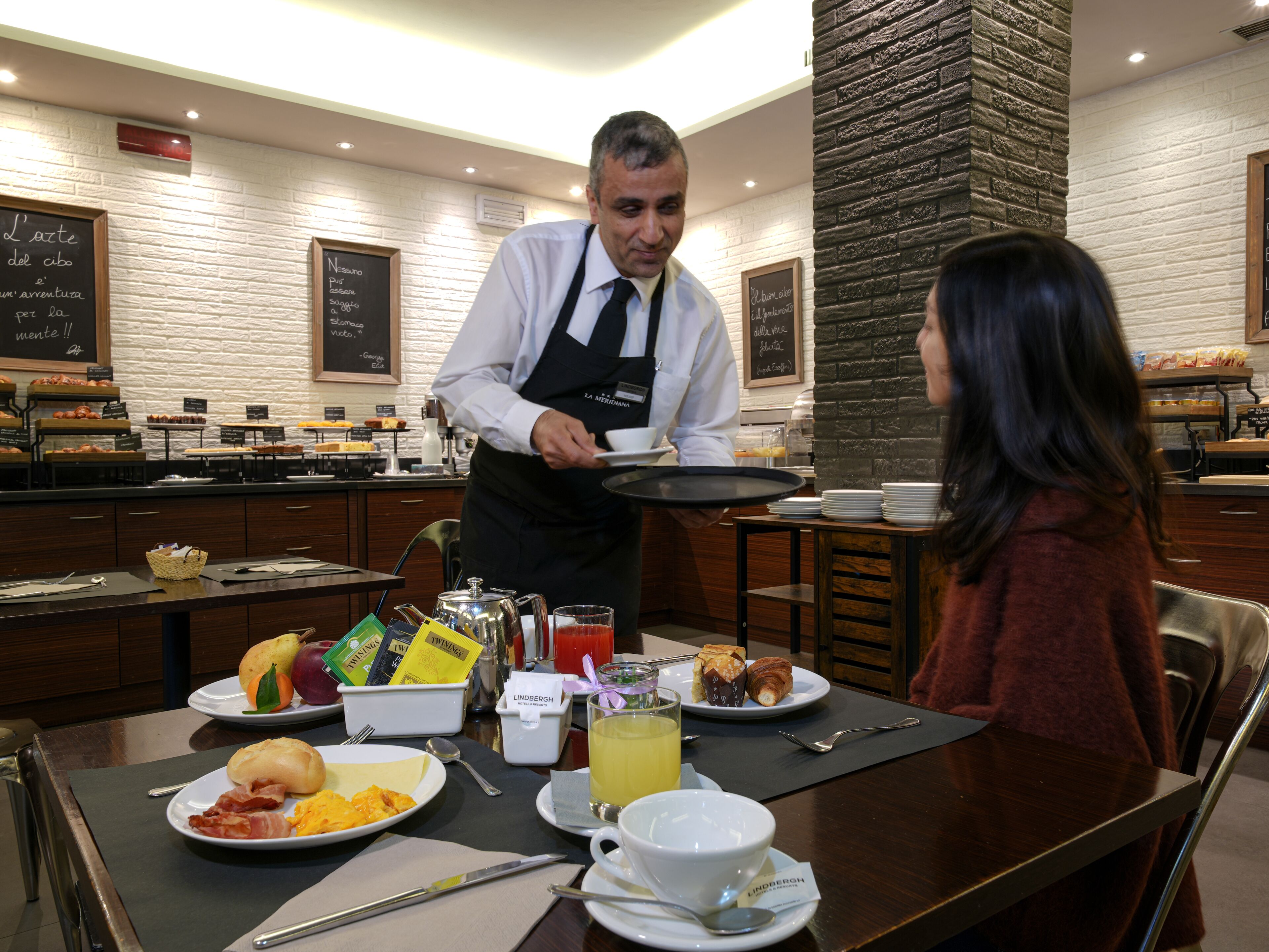 A breakfast setting with a waiter serving a plate to a customer.