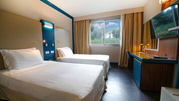 Hotelkamer met twee bedden, een bureau, een flatscreen-televisie, een raam met gordijnen en uitzicht op groen.
