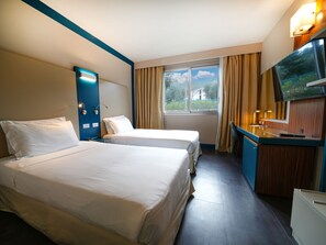 A hotel room with two beds, a desk with a flat-screen TV, a window with curtains, and a view of greenery outside. - La Meridiana Bleisure Hotel (Perugia)