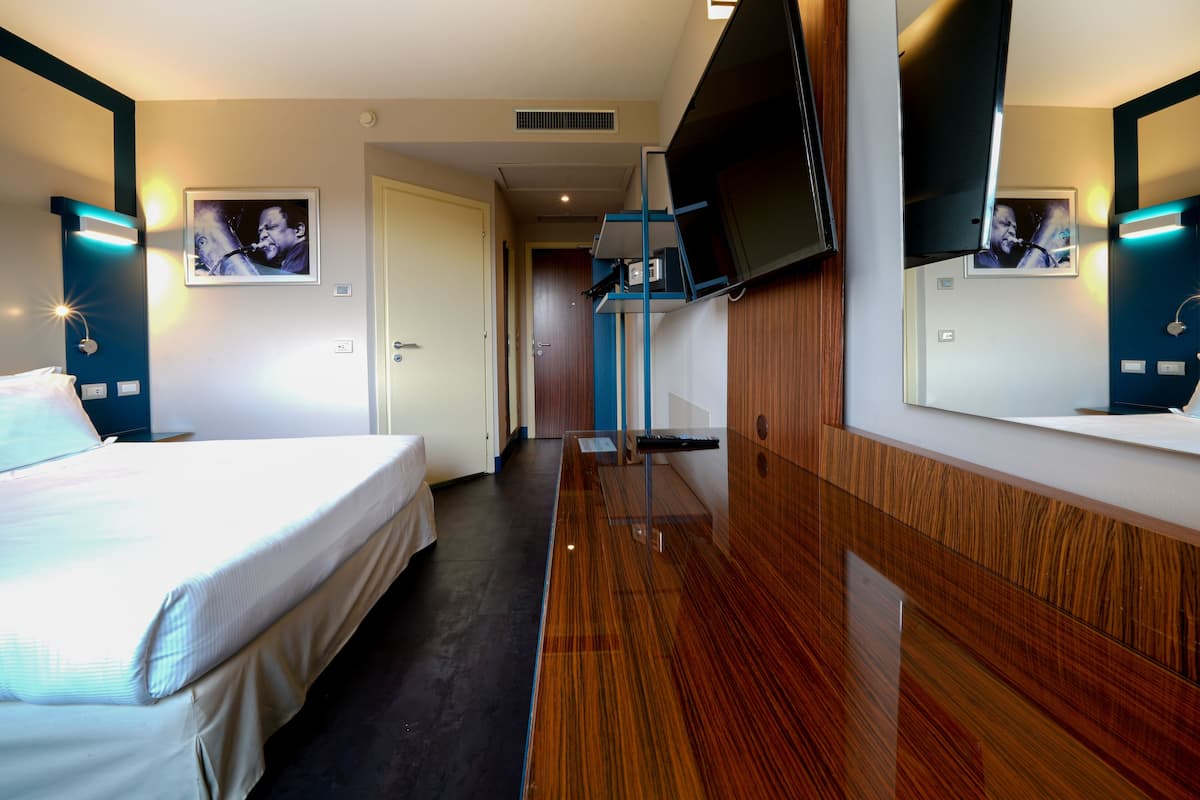 A hotel room with a bed, a TV mounted on the wall, and a wooden panel design.