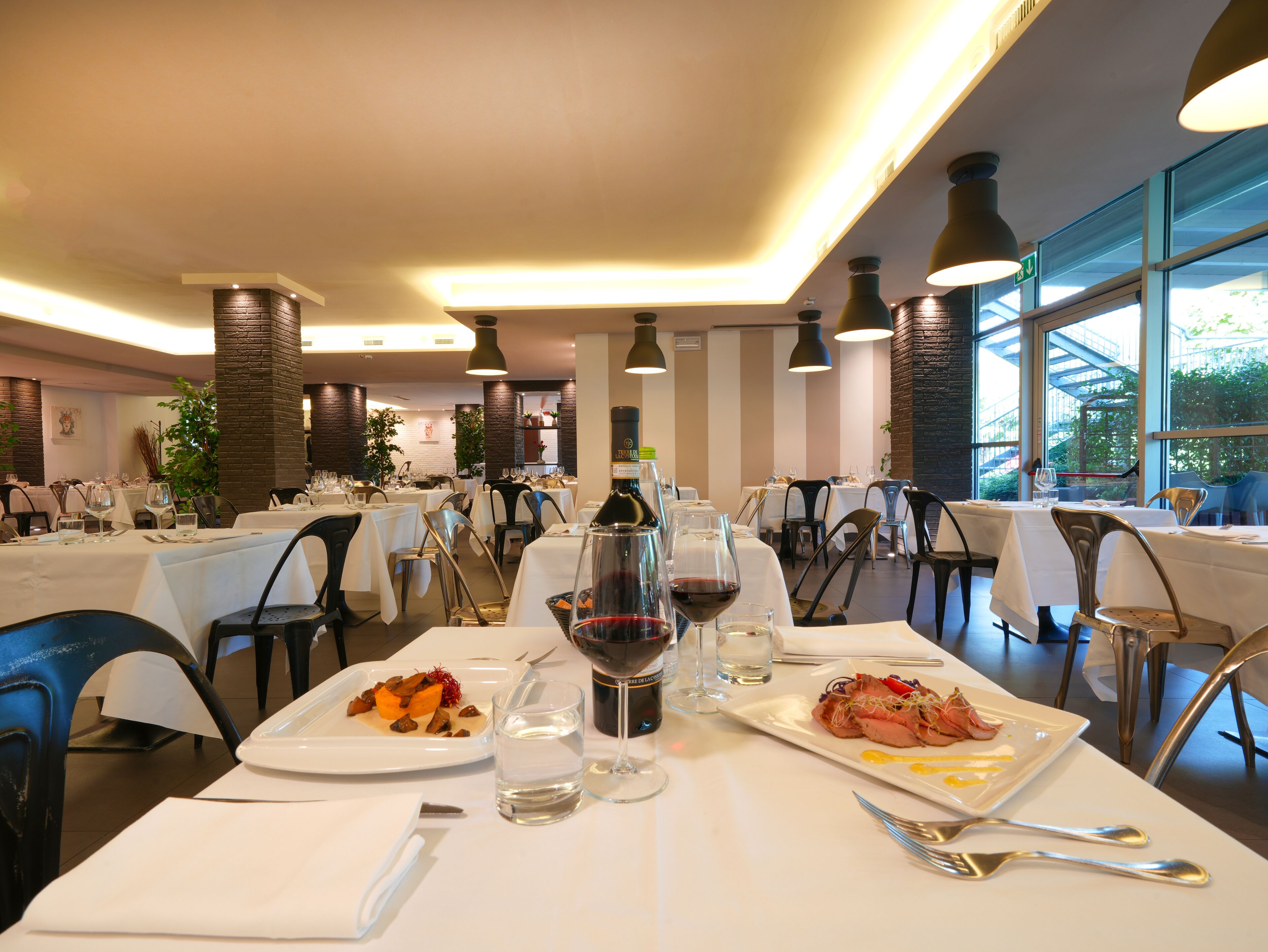 A restaurant with multiple tables, each set with white tablecloths, wine glasses, and plates of food.