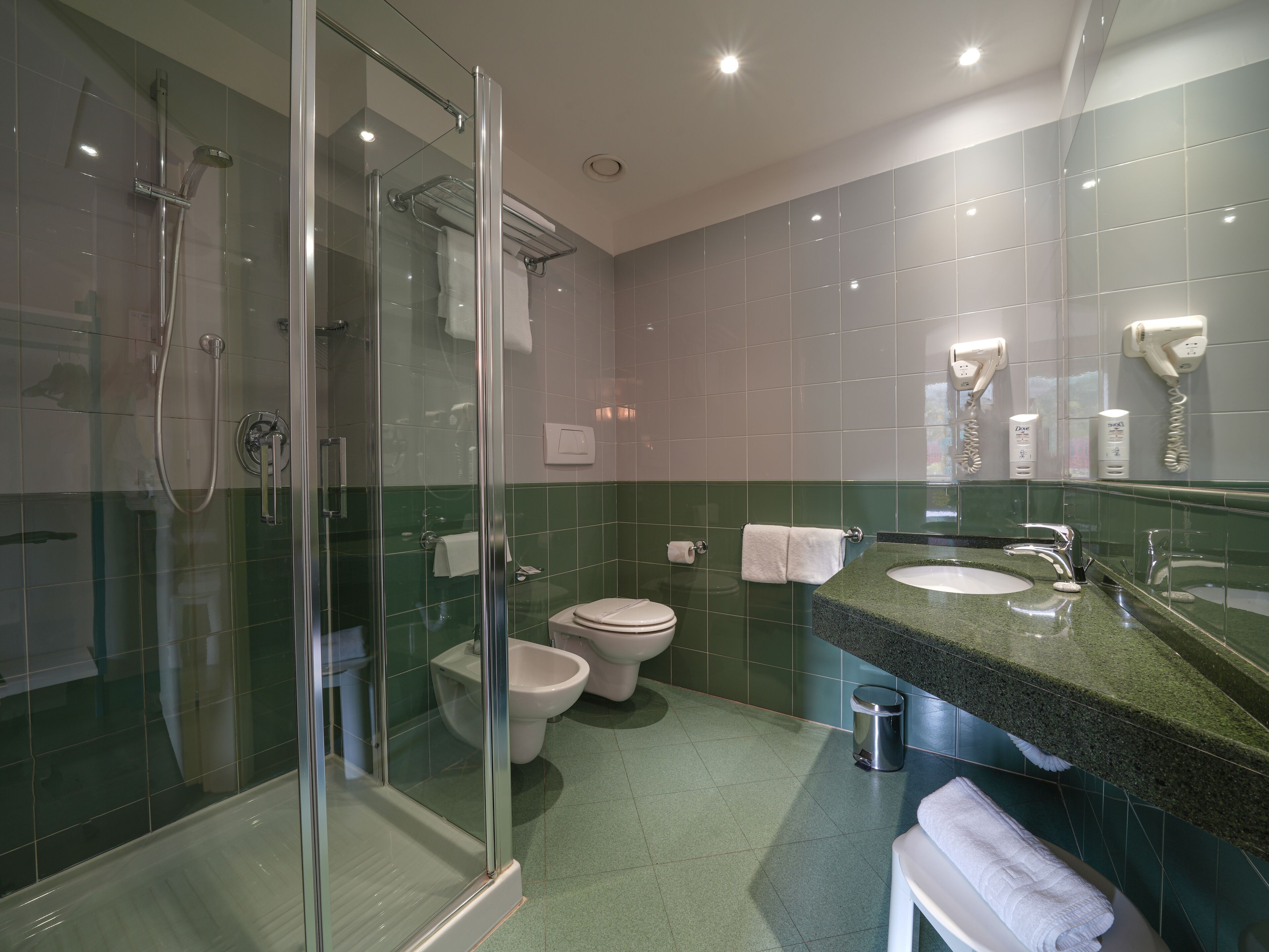 A modern bathroom with a glass-enclosed shower, a toilet, and a sink with a green countertop.