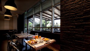 A restaurant with a wooden table set for breakfast, large windows, and hanging pendant lights.