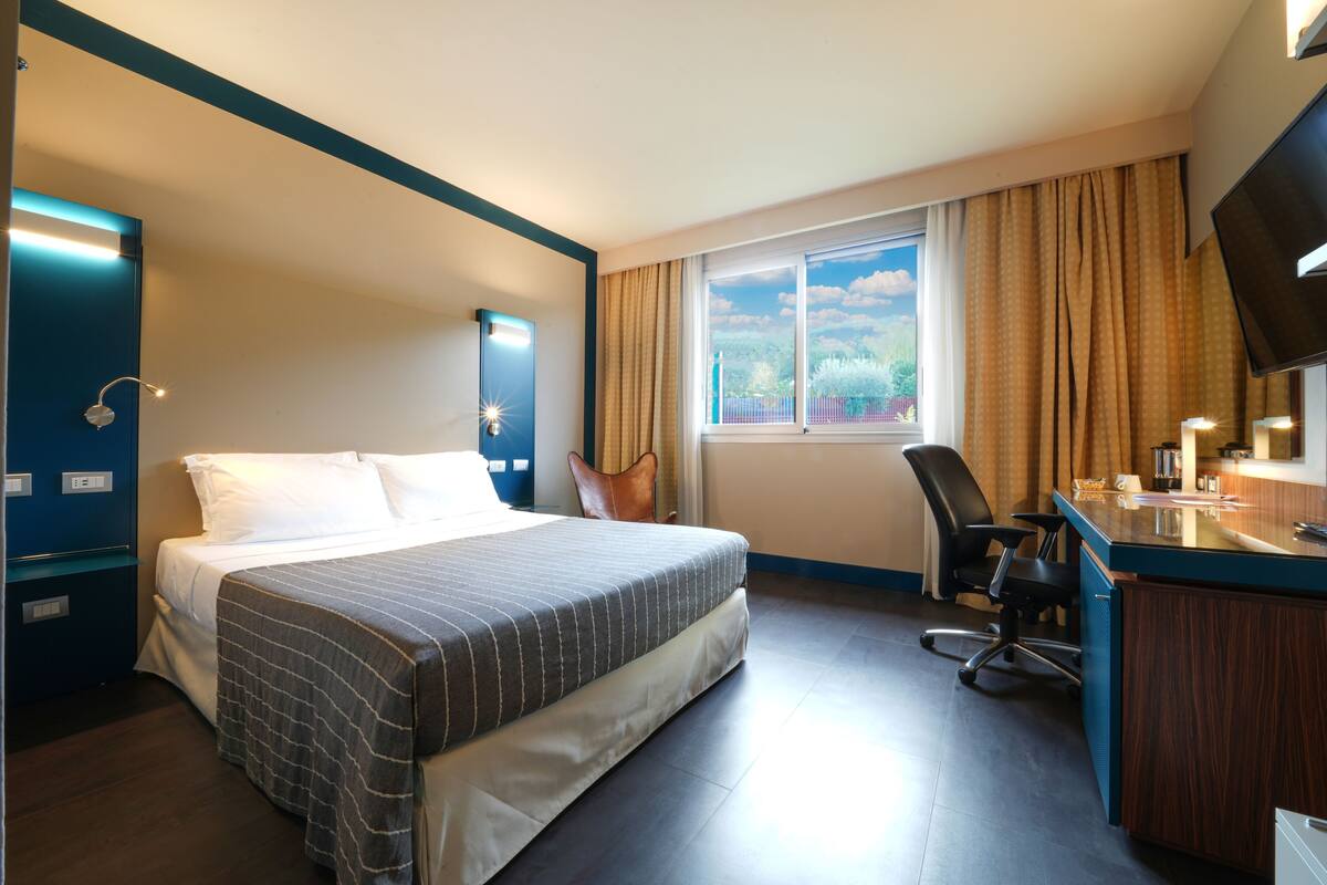 A hotel room with a bed, desk, chair, and a window with curtains.