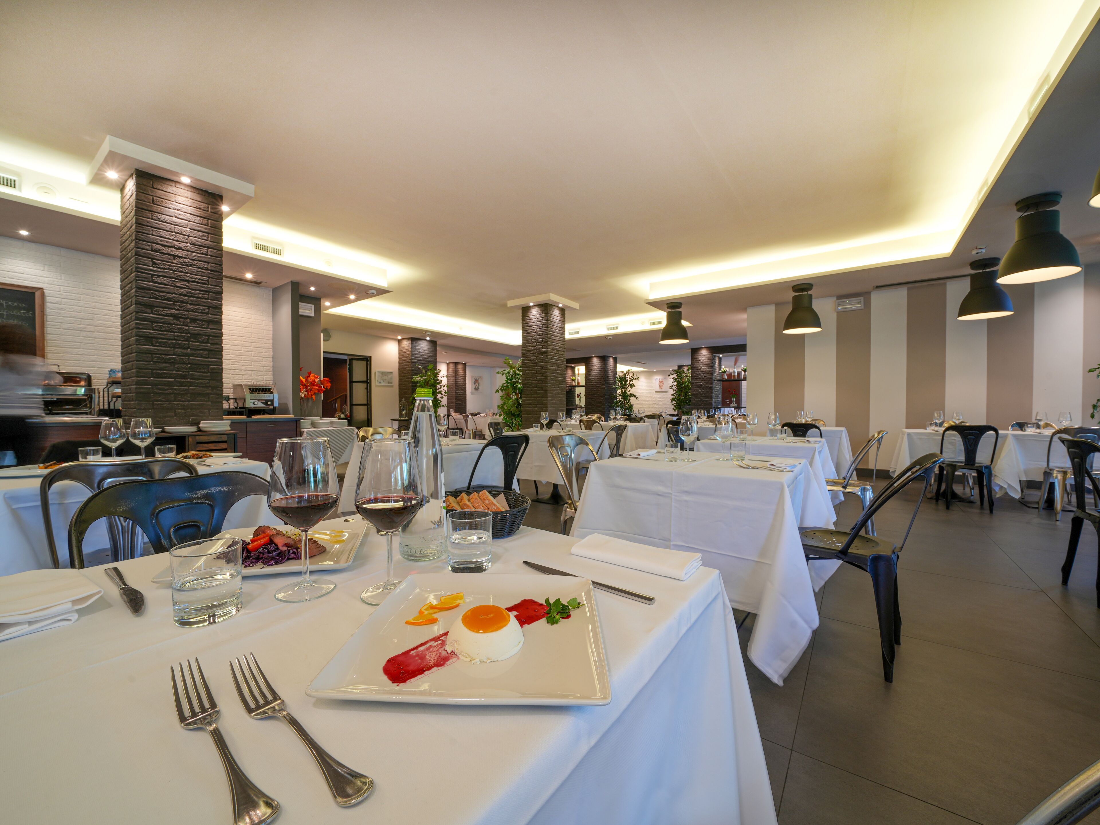 Un ristorante con diversi tavoli apparecchiati per la cena, con tovaglie bianche e arredamento moderno.