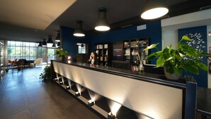 A modern hotel reception area with a reception desk, seating area, and a large window providing natural light.
