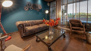 A modern living room with a blue brick wall, leather sofa, a glass coffee table, and a decorative clock.