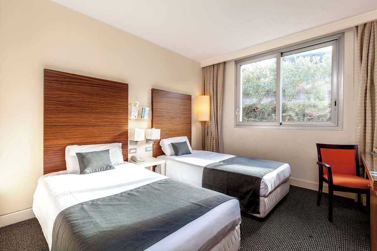 A hotel room with two beds, a desk, a chair, and a window with curtains.