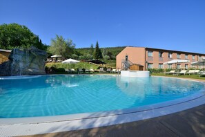A swimming pool with a waterfall feature, lounge chairs, and a building with a balcony in the background. - La Meridiana Bleisure Hotel (Perugia)