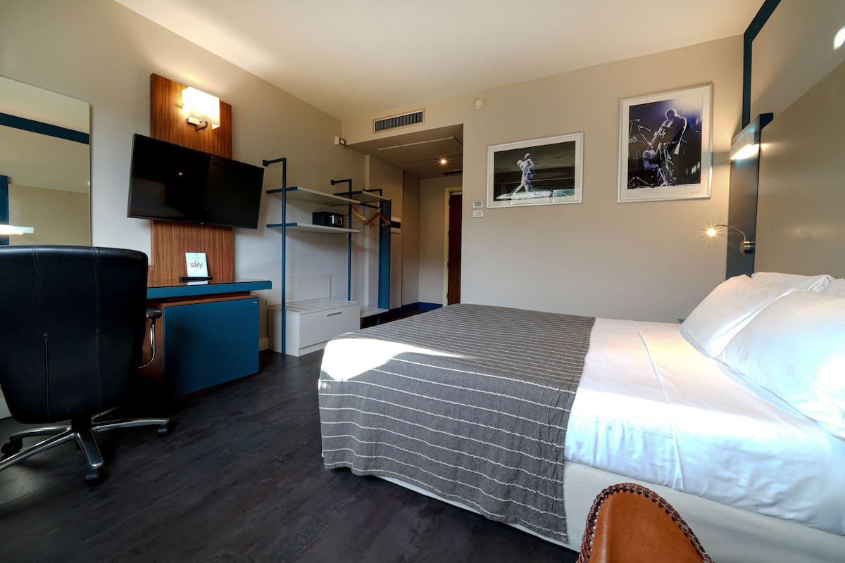 A hotel room with a bed, a desk with a chair, a television, and a wardrobe.